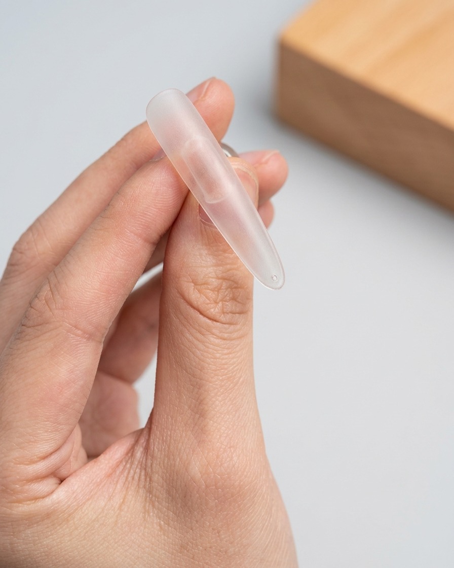 A brush applying a layer of shimmery cat-eye gel to the upper portion of a clear nail tip.