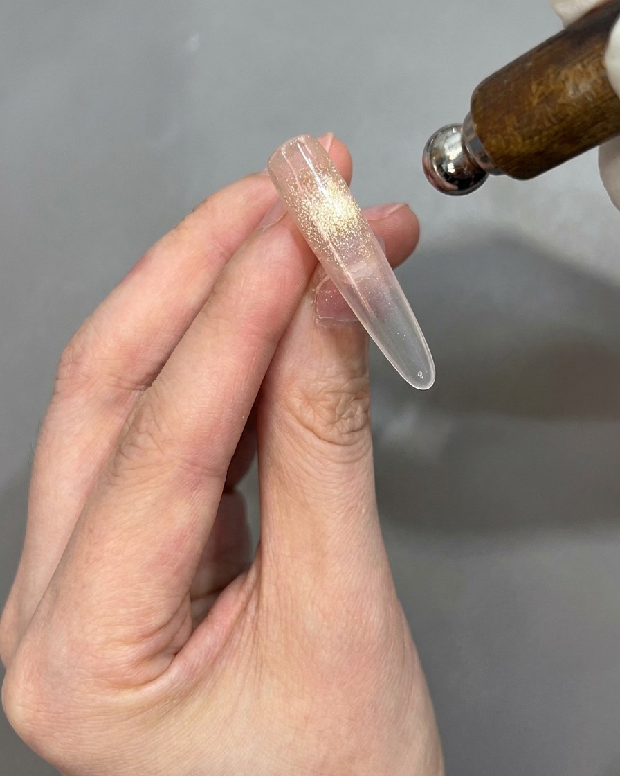 A magnet being held near a nail tip to activate the cat-eye effect, with the nail tip positioned for flipping.