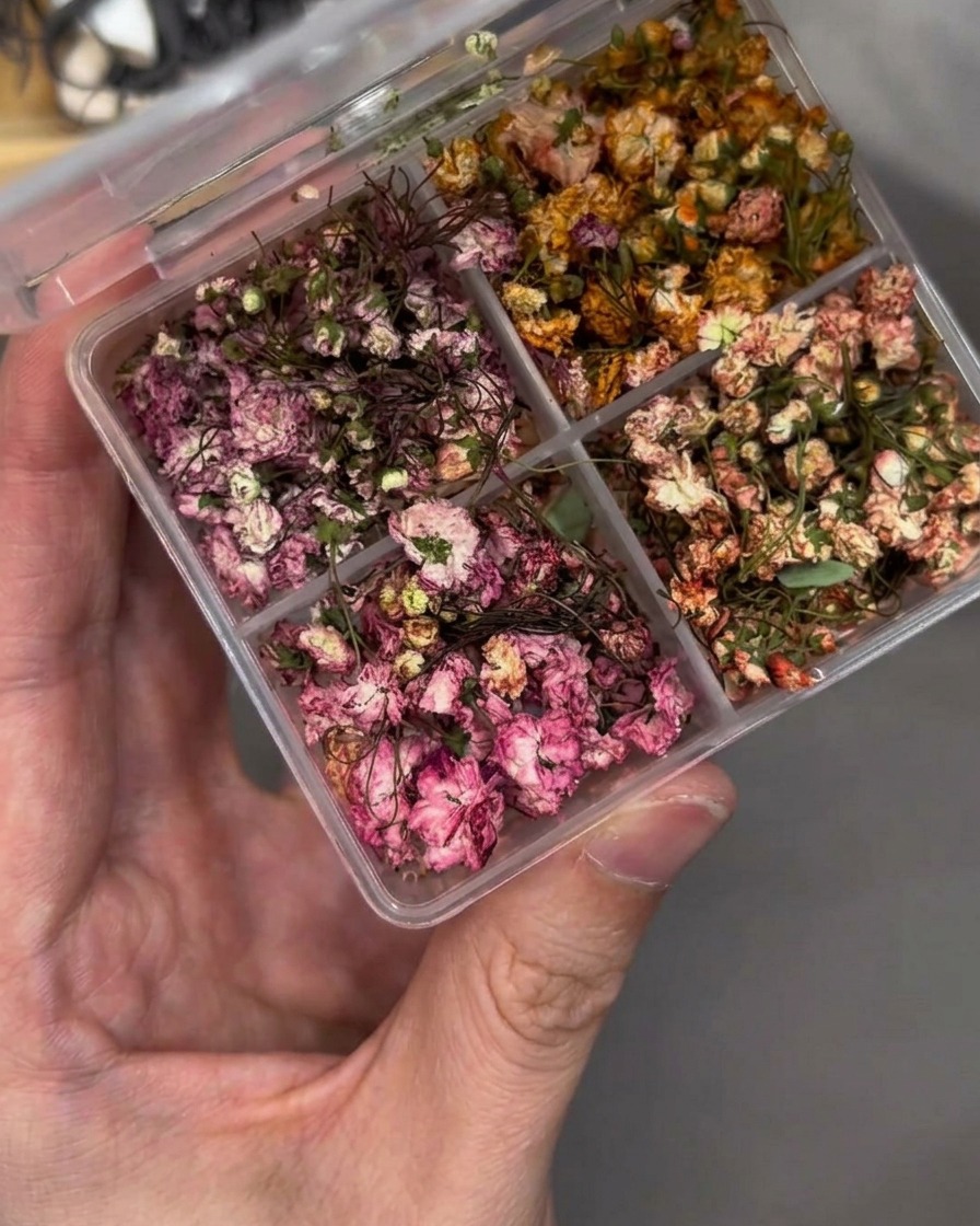 Tweezers carefully placing a small dried flower onto a nail tip.