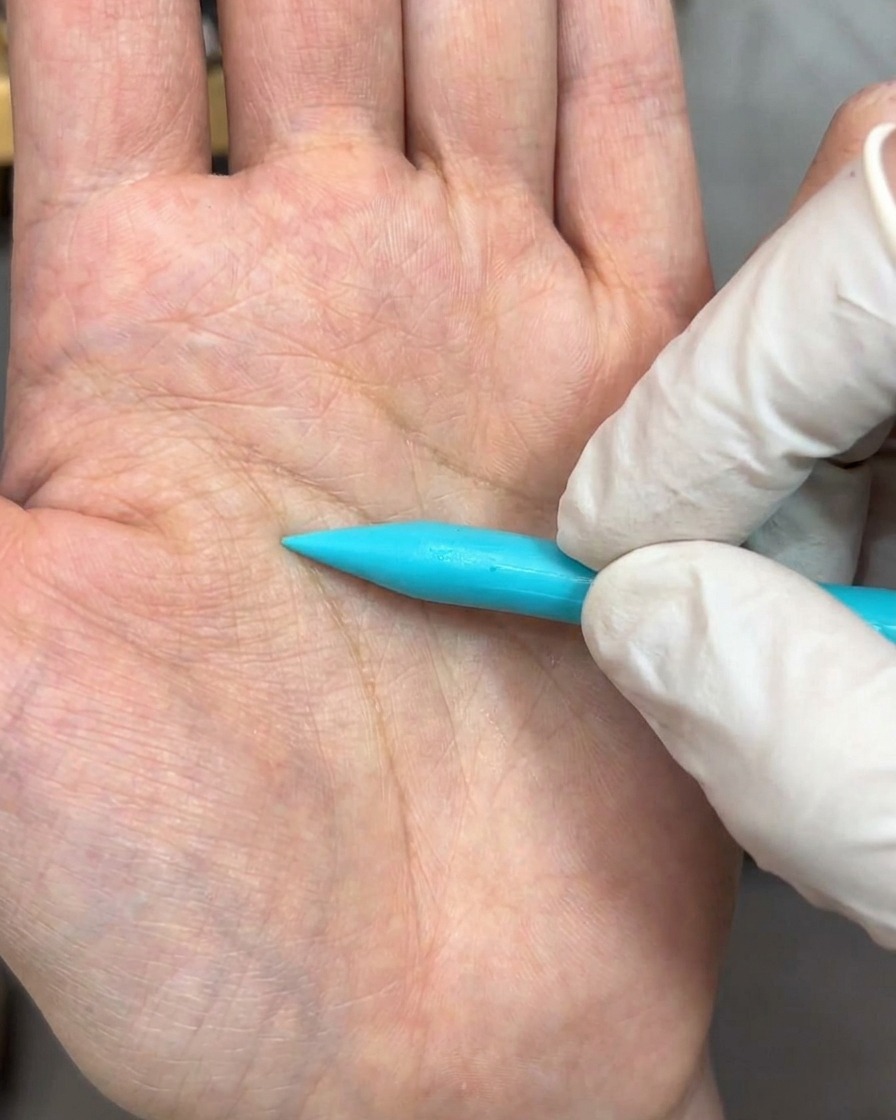 A sculpting tool pressing a bead of white gel flat on a surface, forming a delicate petal shape.