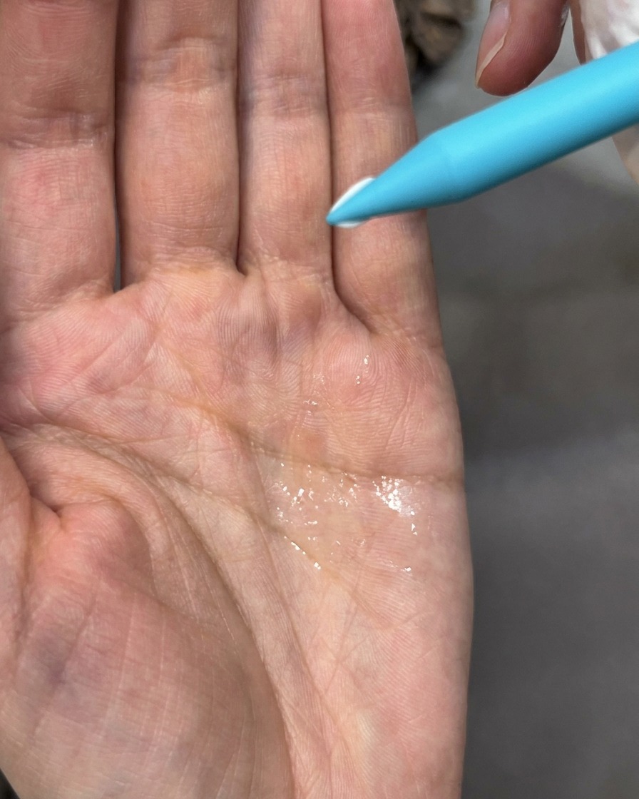A brush tool adjusting a small, white sculpted petal on a nail surface with embedded dried flowers.