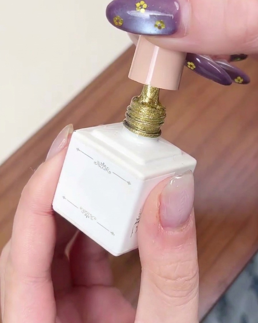 A brush applying a layer of shimmery gold cat-eye gel to a fingernail.
