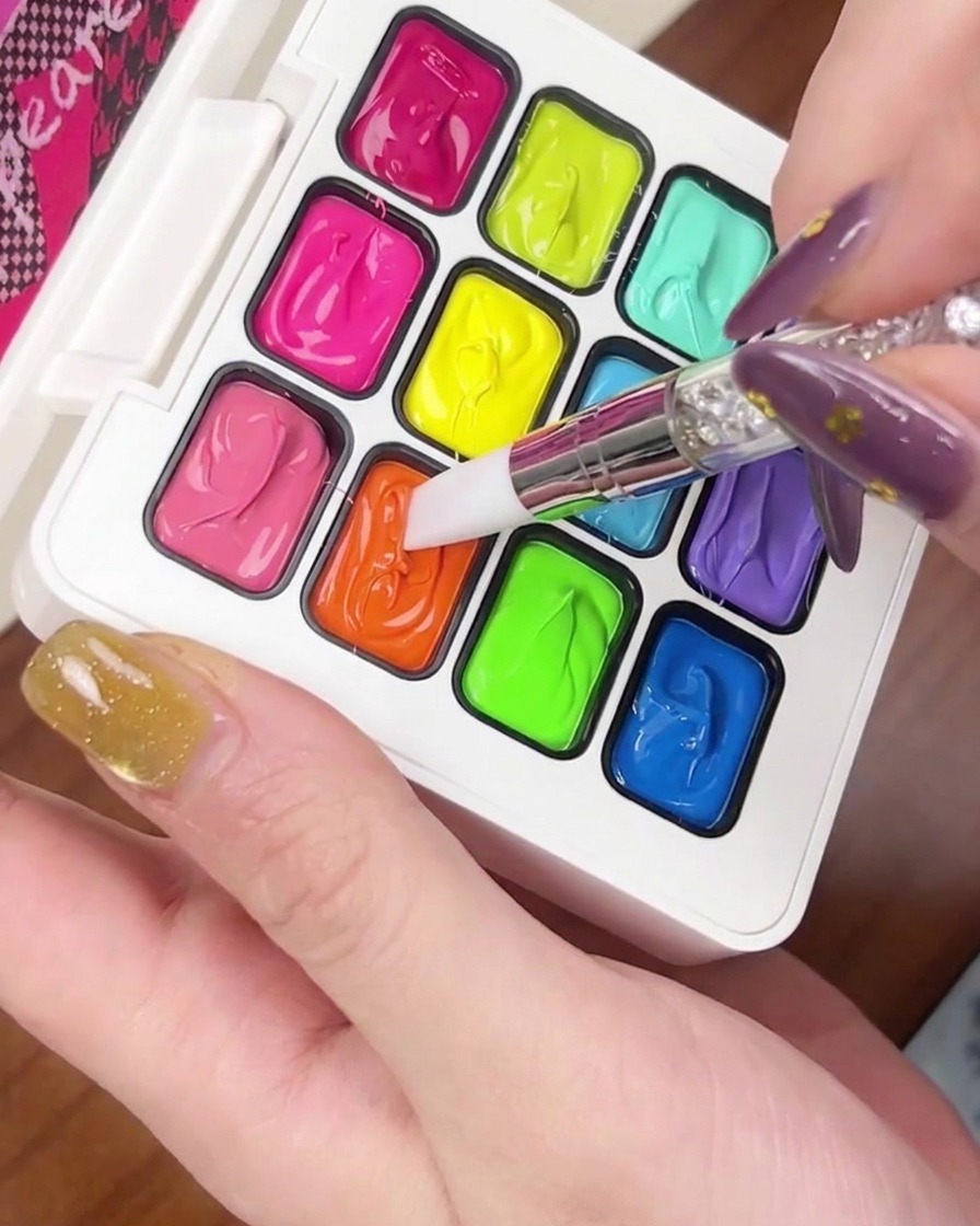 A small dollop of bright orange gel polish being placed on the tip of a gold cat-eye nail.