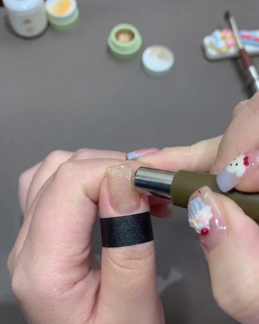 A cylindrical magnet being moved around the edges of a fingernail painted with sparkling light gold cat-eye gel polish.