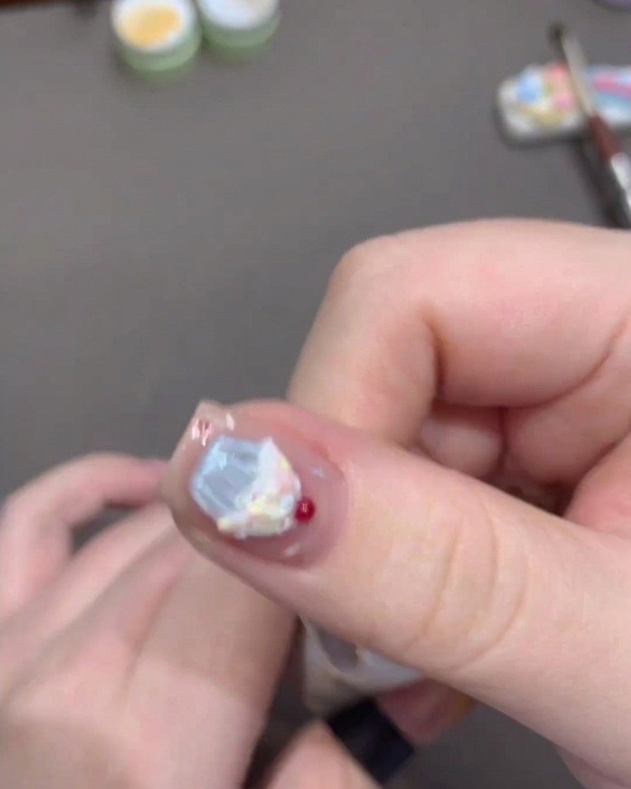 A brush applying a clear, glossy top coat over a sunset-orange gradient nail design.