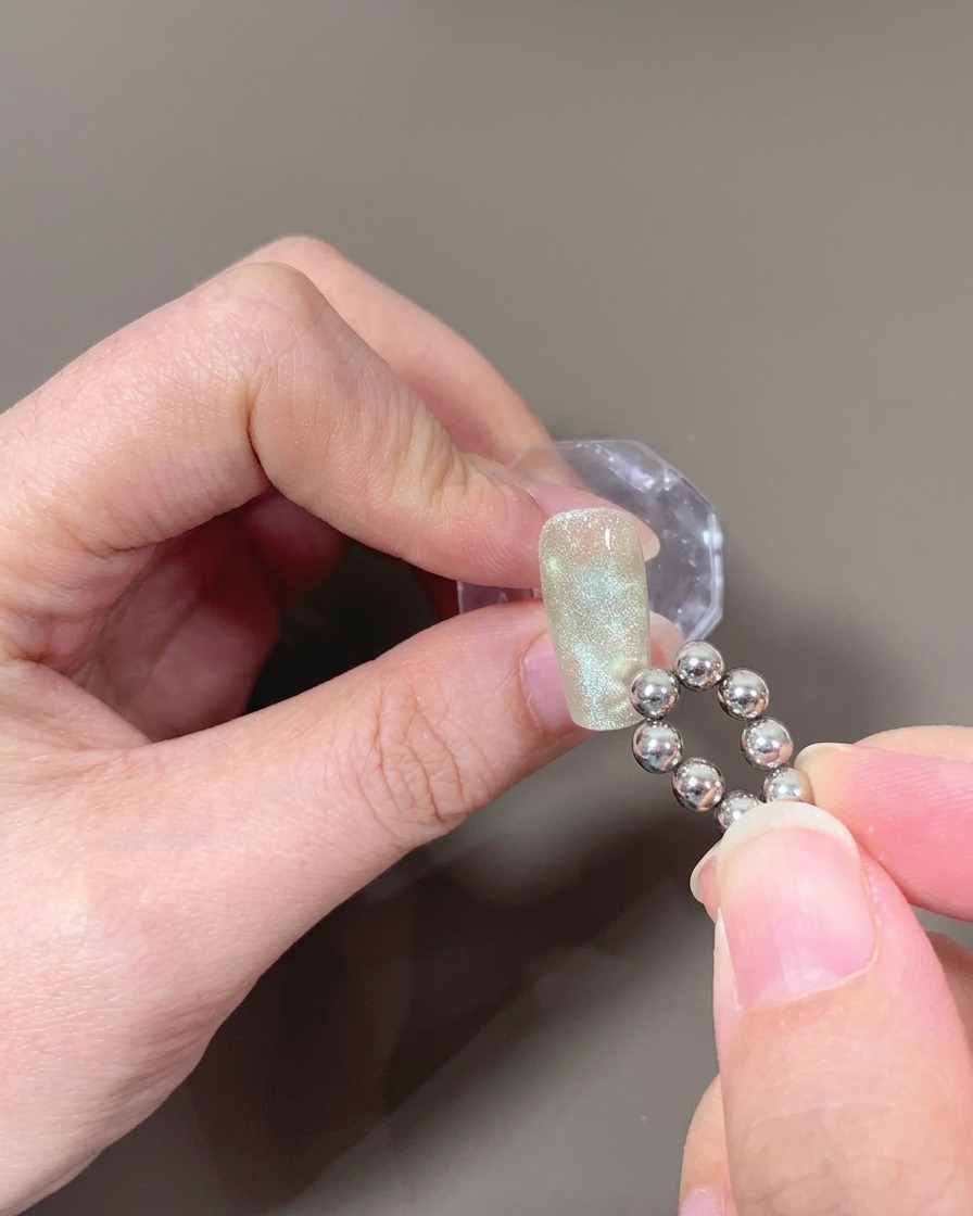 A close-up of a nail with uncured cat-eye gel, with a ball-tipped magnet creating a wave pattern.