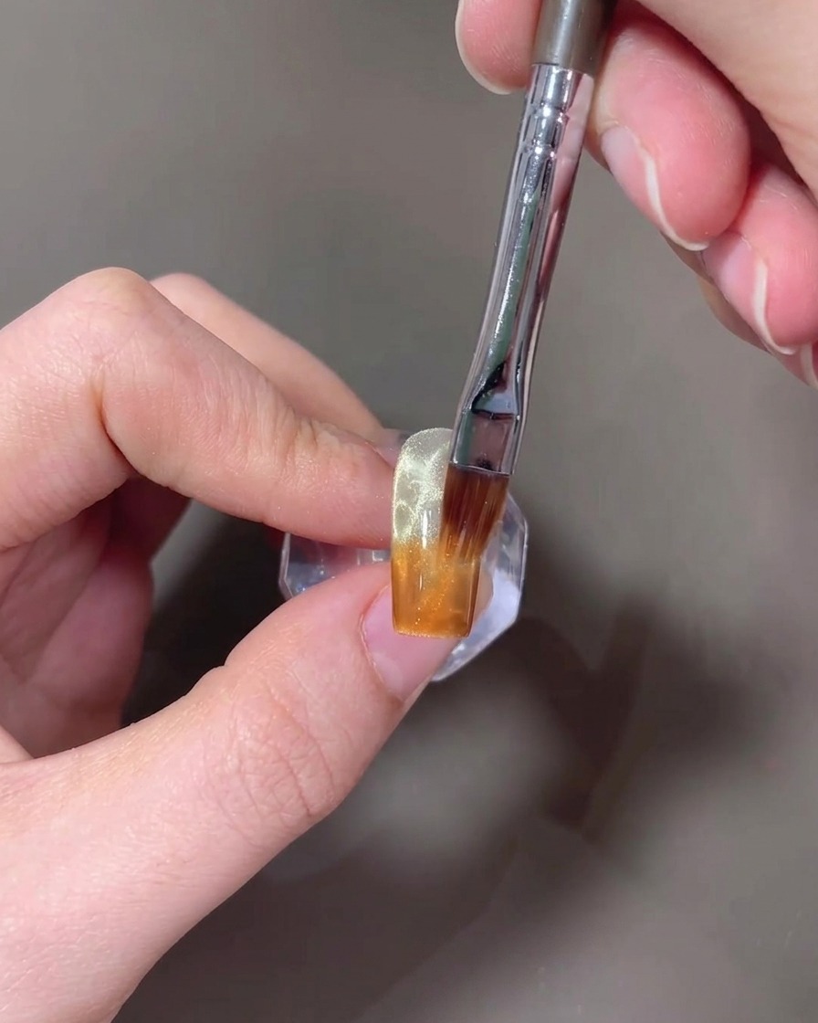 A brush blending amber gel upwards on a nail to create a gradient.
