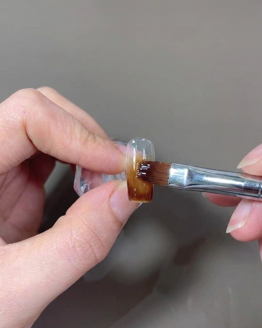 A brush applying a final layer of glossy top coat to the nail.