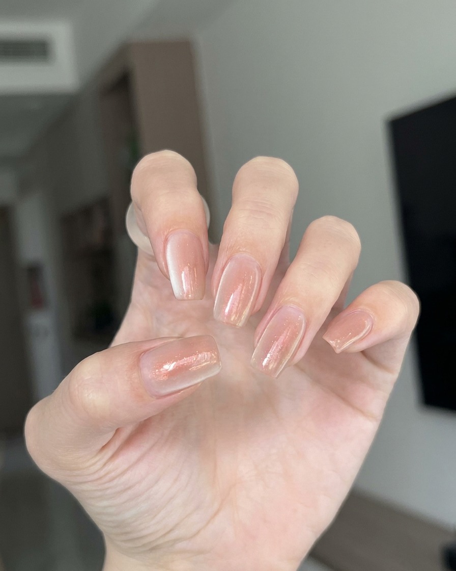 A close-up of a brush applying a thin, clear layer of builder gel onto a clear nail extension.