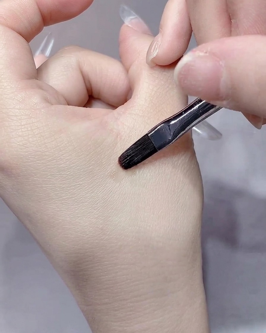 A thin liner brush carefully smoothing the edges of the builder gel near the cuticle area.