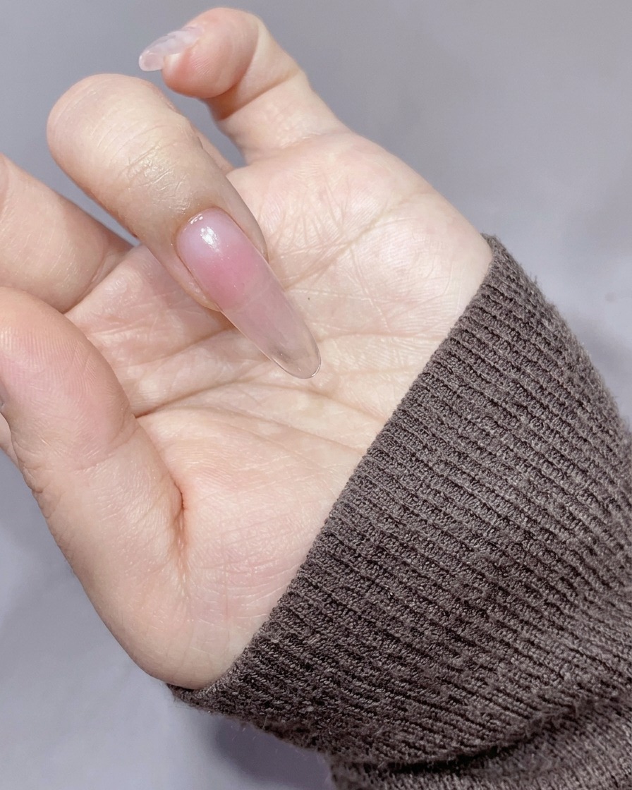 A makeup sponge patting a soft, peachy-orange color onto the center of the nail.