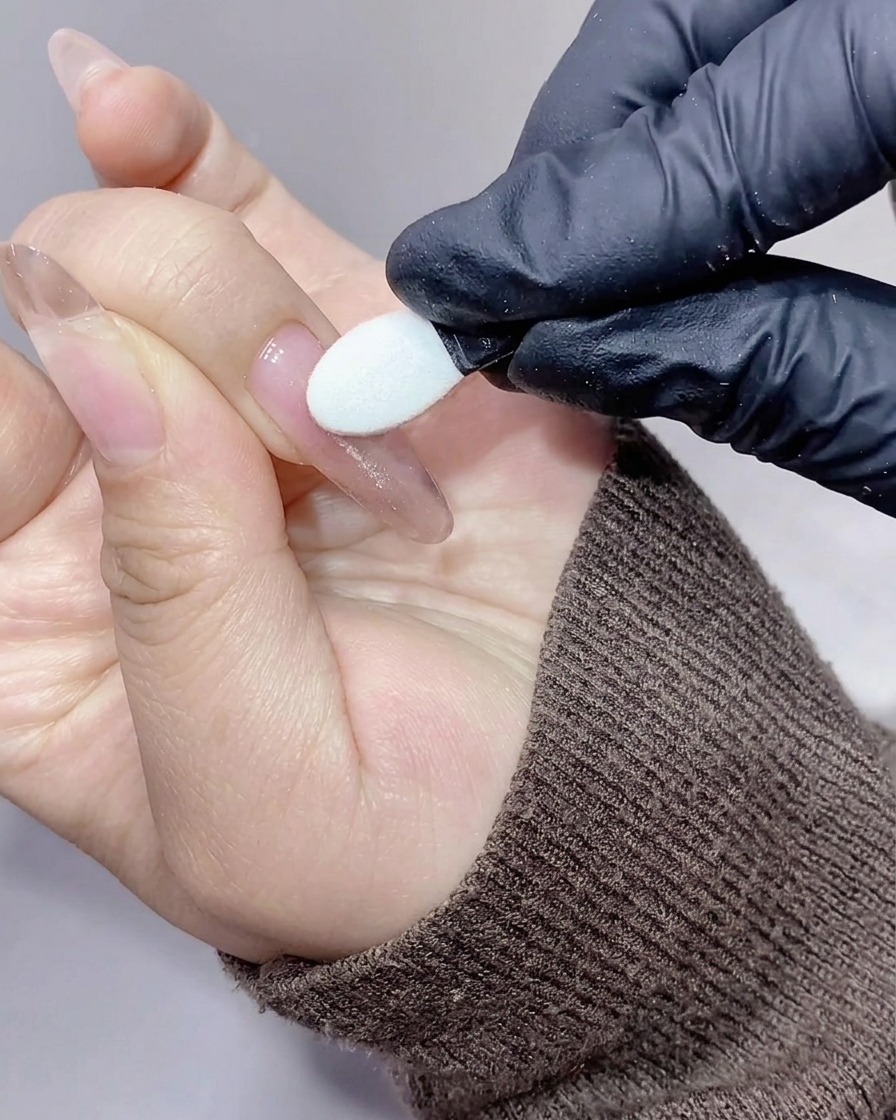 A silicone applicator rubbing shimmery, iridescent aurora powder onto the surface of a nail.