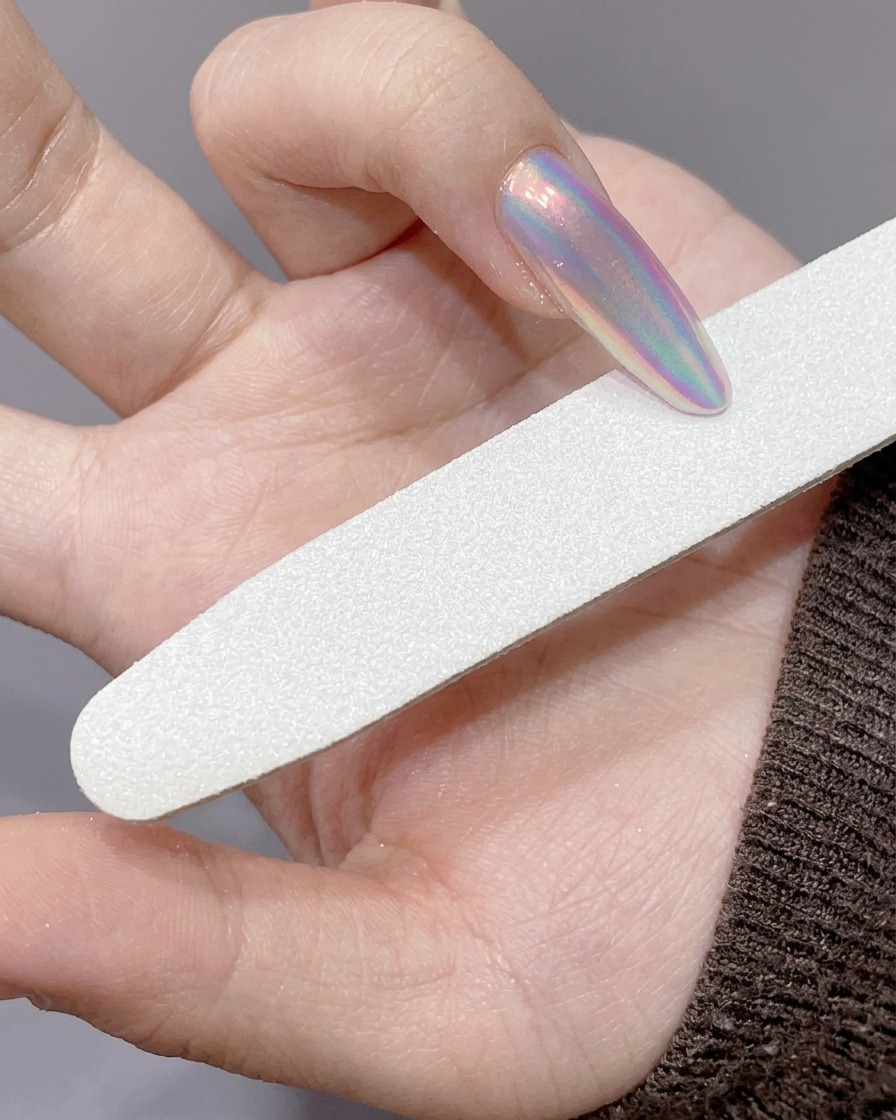 A hand file being used to refine the edge of a long, chrome-powdered nail.