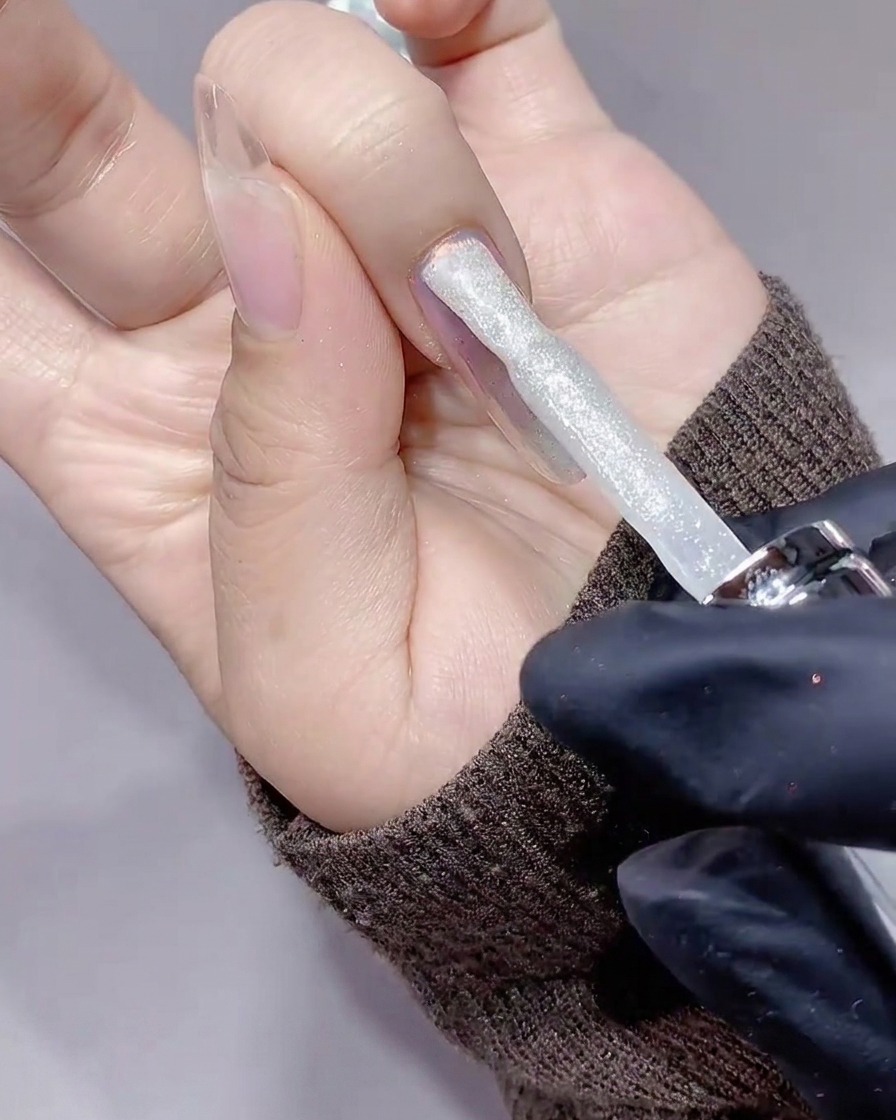 A brush applying a layer of sparkly, silver crushed diamond gel onto a nail.