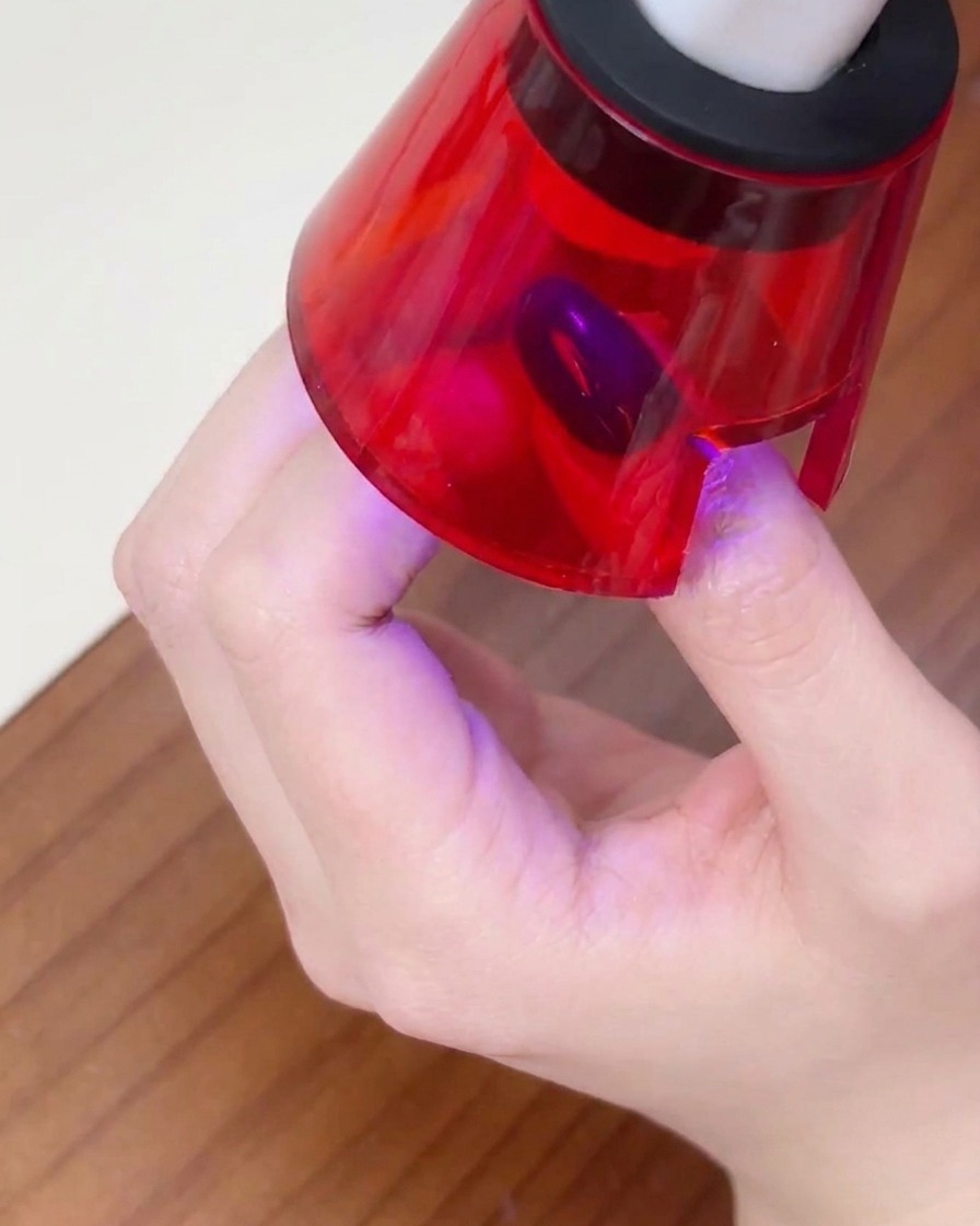 A hand positioned inside a small UV nail lamp, with the finger centered to cure the polish.