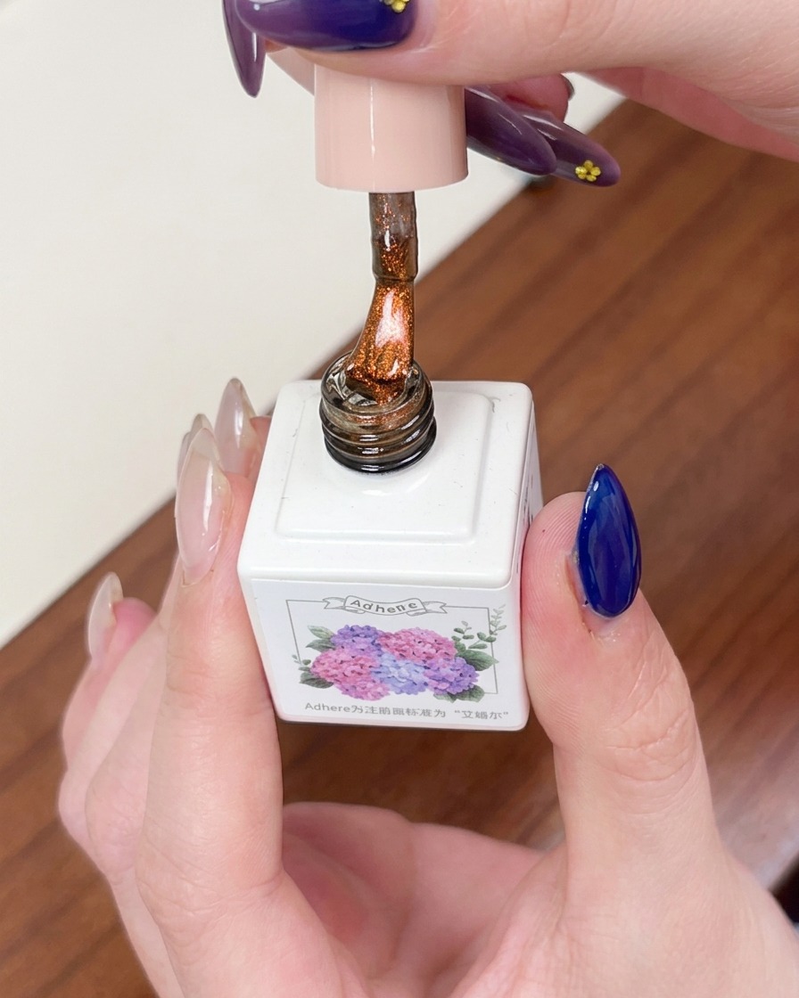 A brush applying a coat of sheer amber-colored magnetic cat eye gel over the dark blue base.