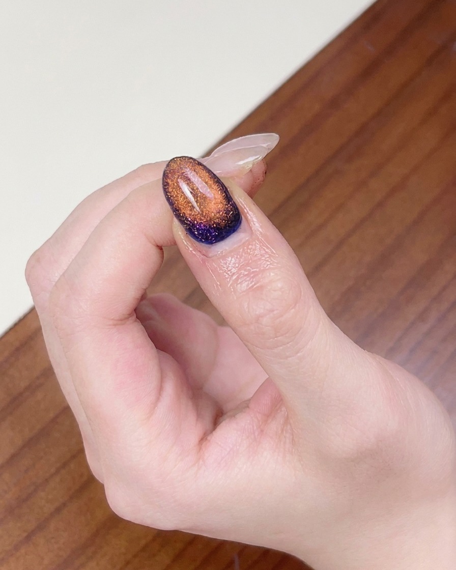 A finger placed under a UV nail lamp to cure the completed magnetic cat eye nail art.