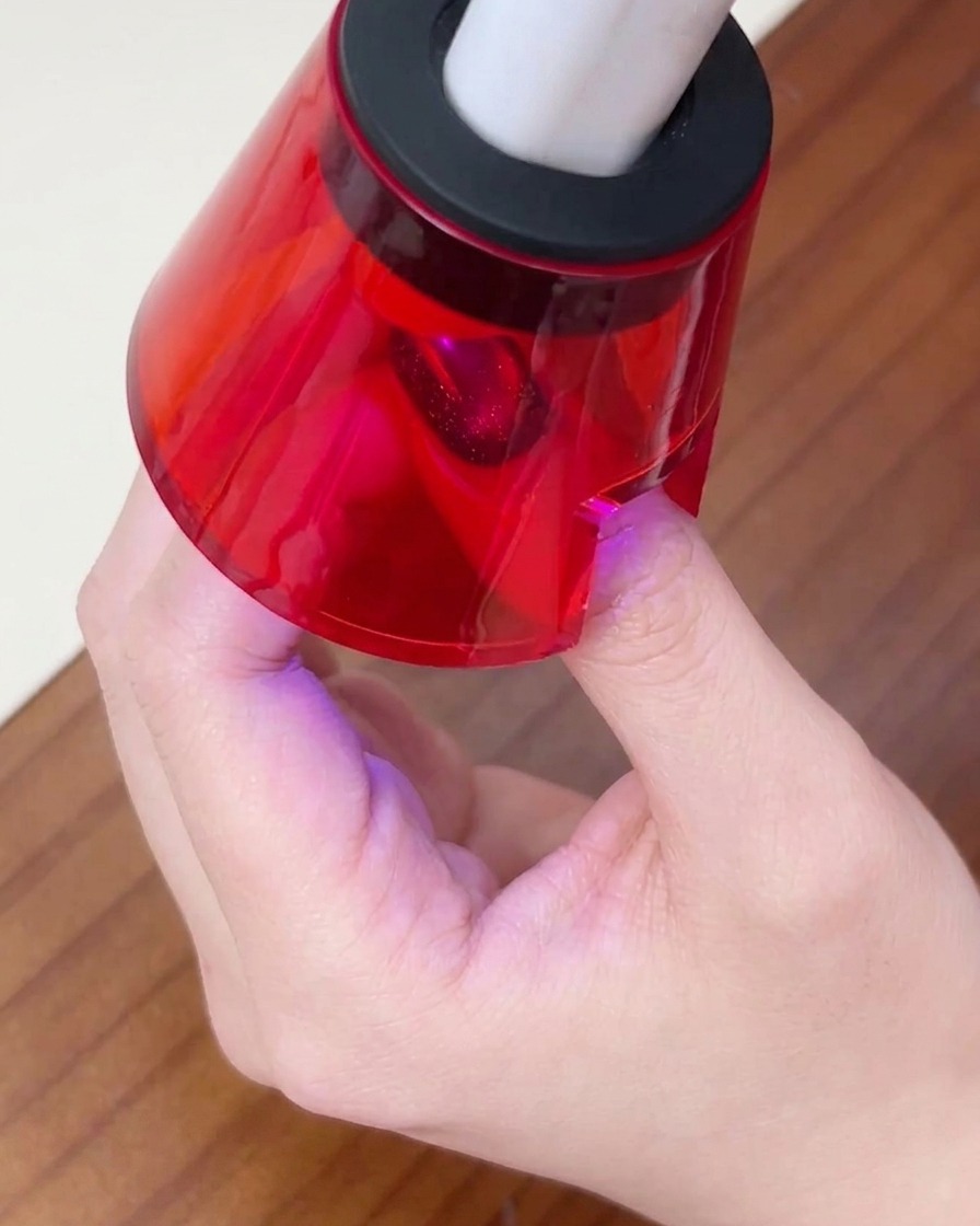 A persons finger resting under a small, red UV/LED nail lamp to cure the final gel layer.