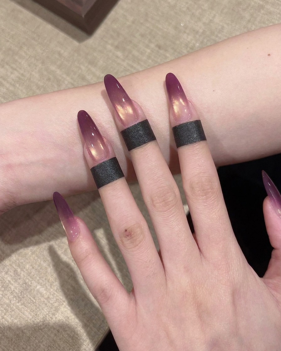 A close-up shot of a small sponge being used to dab and blend the purple gel on a nail extension to create an ombre effect.