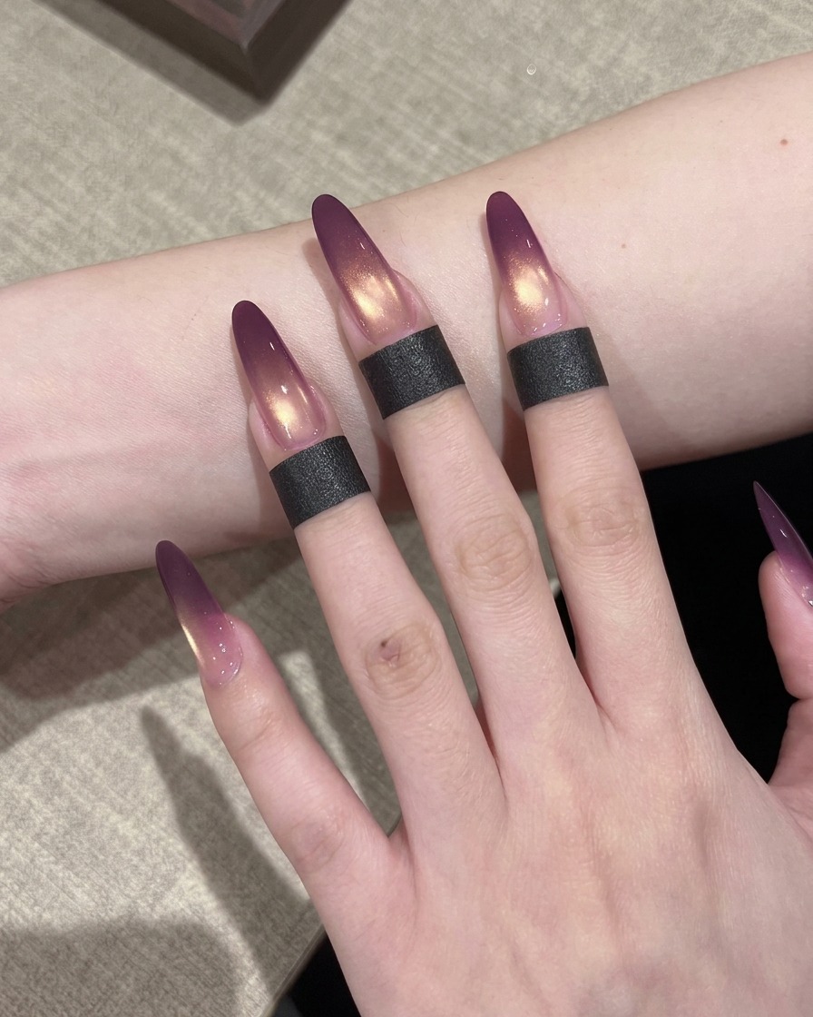 A nail brush applying a coat of shimmering gold cat-eye gel polish over a nail that already has a purple ombre gradient.