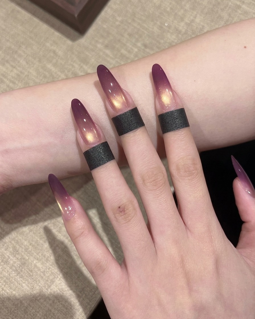 A magnetic wand being held near the side of a wet, gold-coated nail to manipulate the shimmer particles.