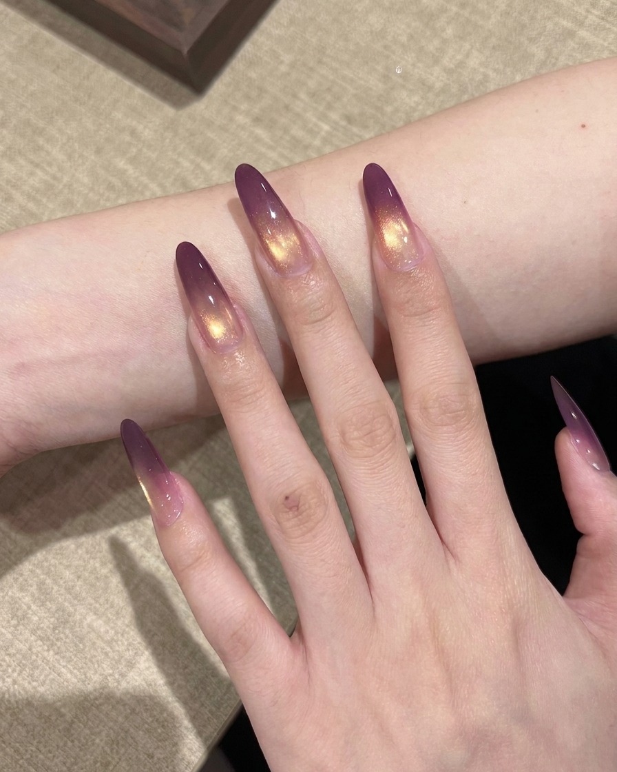 A hand with purple and gold gradient nails placed inside a professional UV nail lamp for curing.