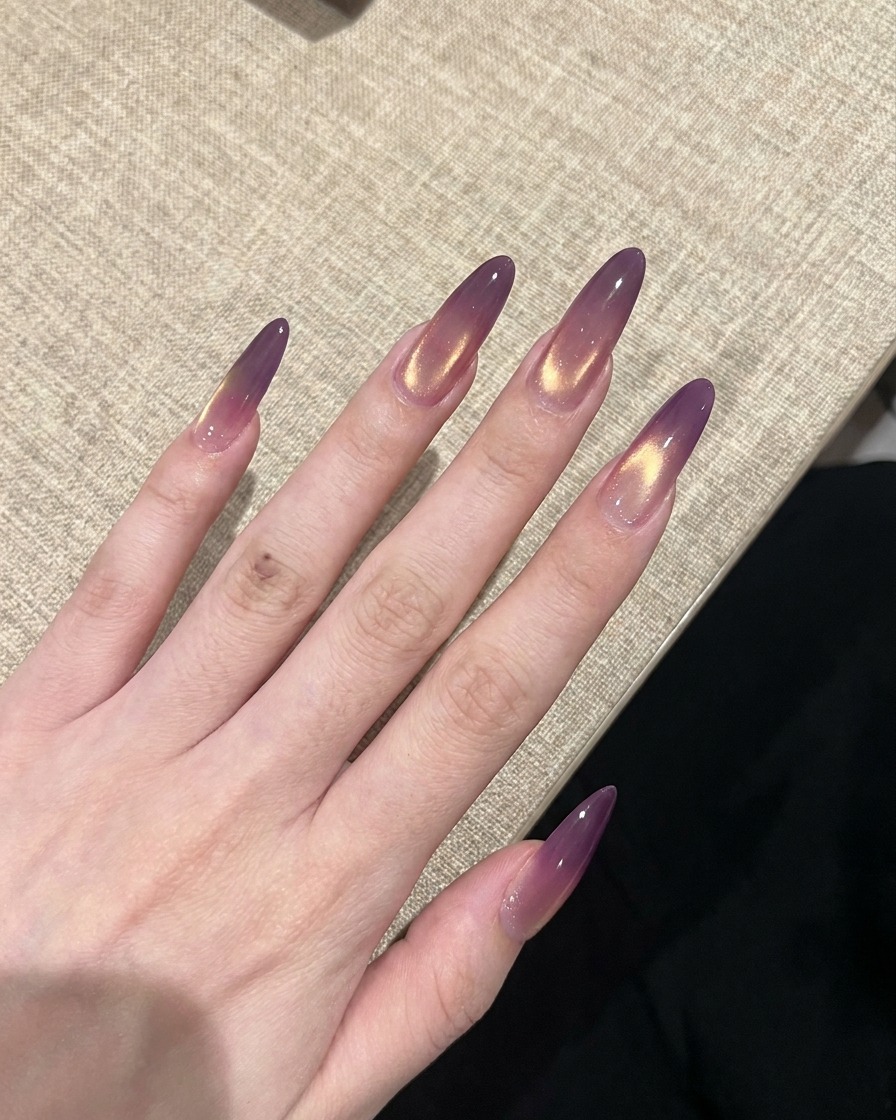 A hand with finished purple and gold gradient cat-eye nails being cured under a UV nail lamp.