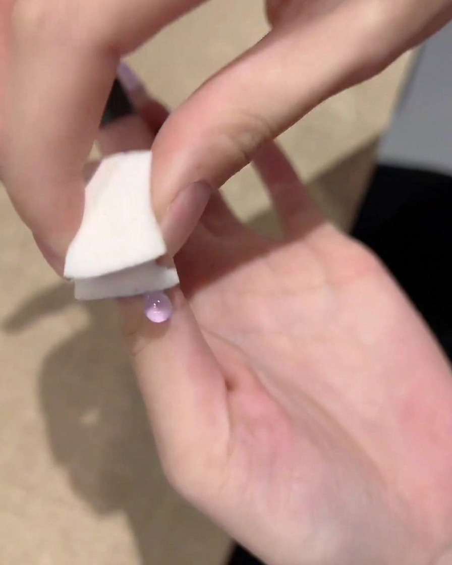 A hand using a small white sponge to tap and blend purple gel polish from the tip of the nail toward the center.