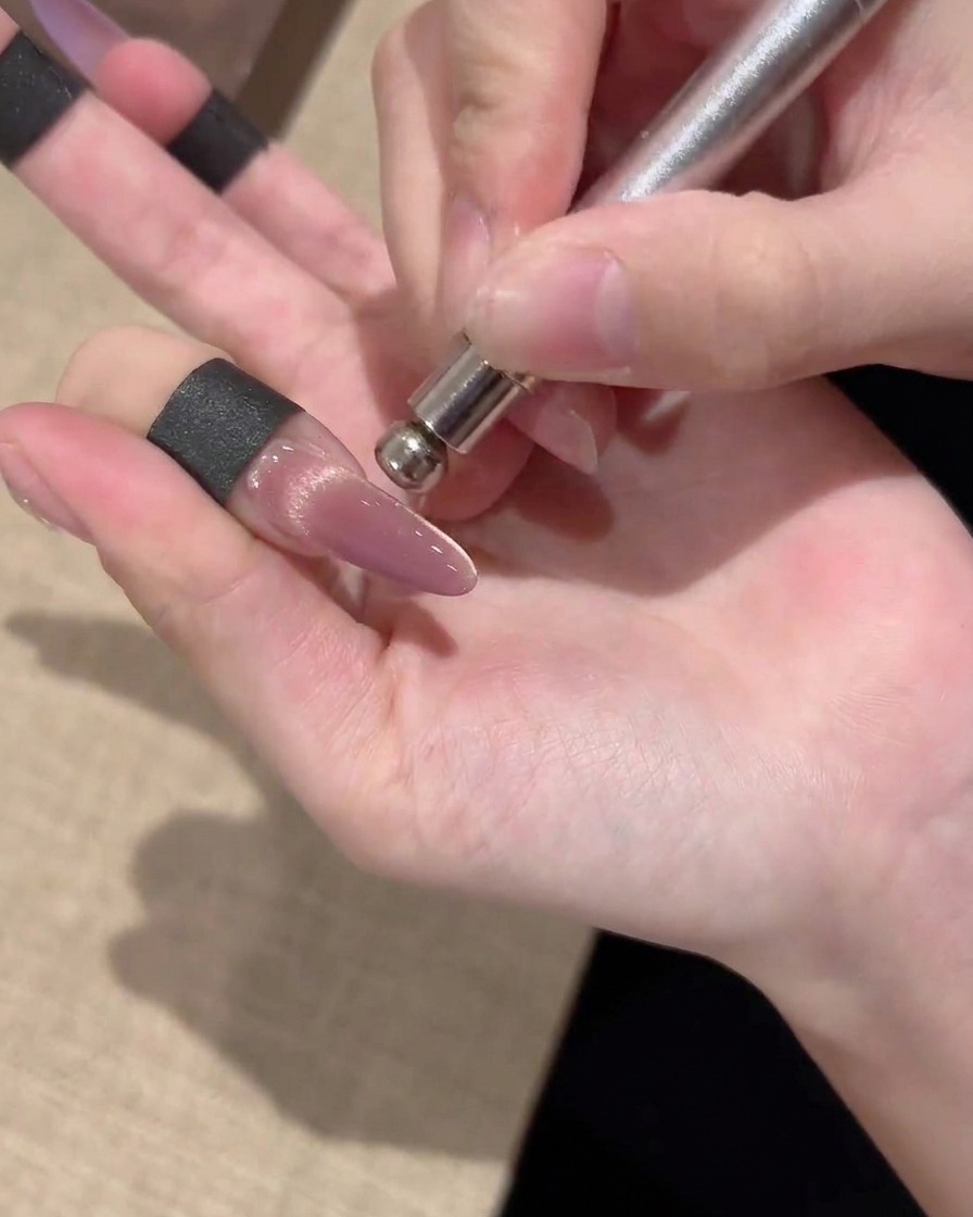 A cylindrical magnetic tool being held alongside a nail, guiding gold magnetic particles into a bright center band.