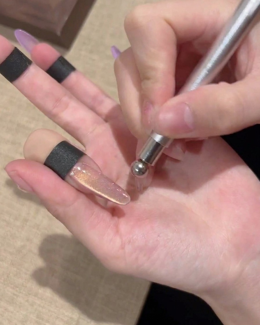 The ball-tip of a magnetic wand creating a circular swirl pattern on a cat-eye gel nail.