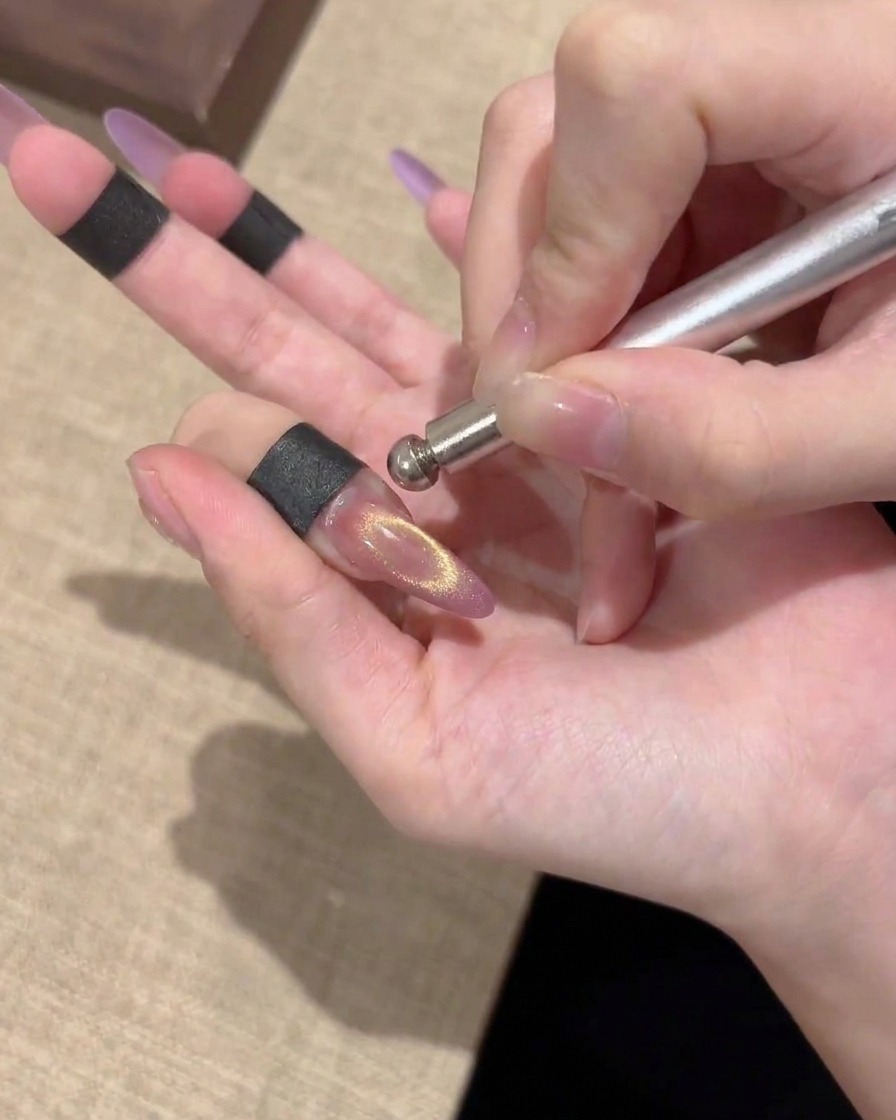 A close-up of a finished magnetic cat-eye nail showing a bright, centered gold shimmer.