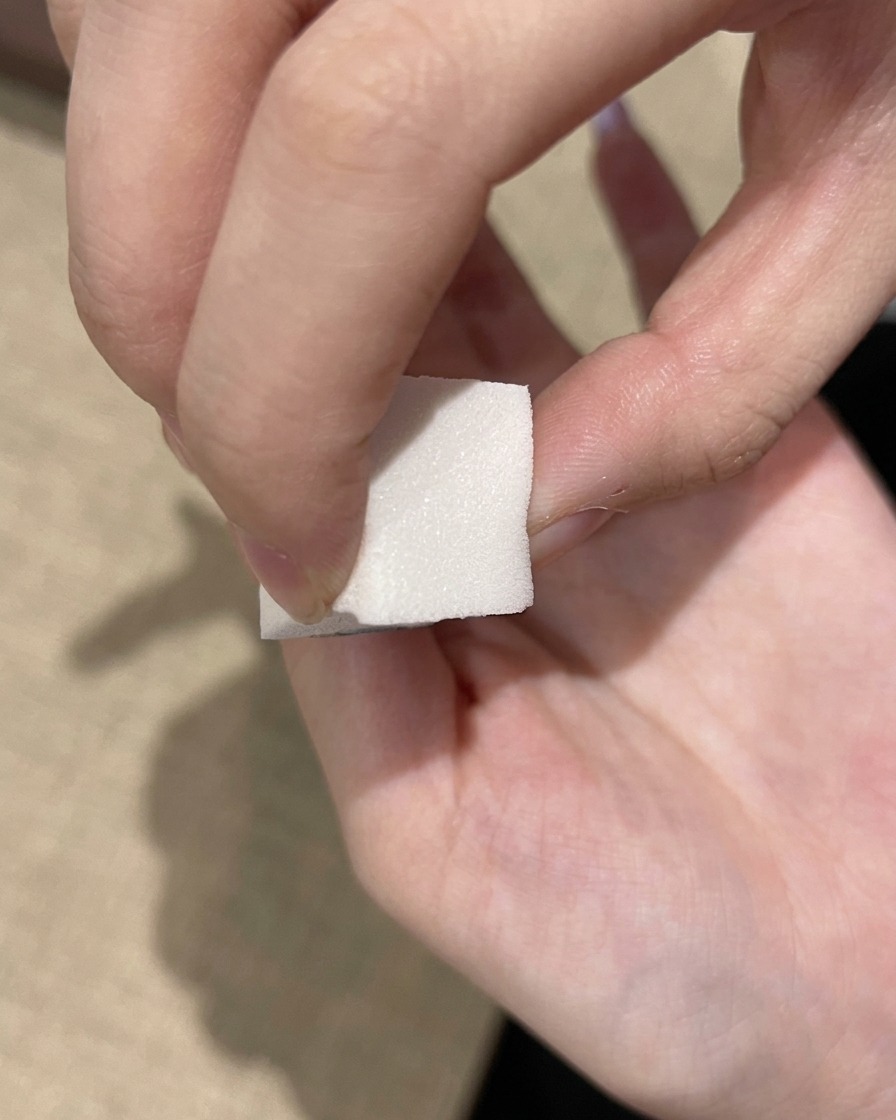 A white makeup sponge dabbing a deep purple gel polish onto the free edge of a nail.