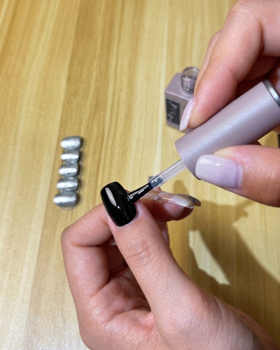 Applying a clear layer of no-wipe top coat onto the cured black gel nail.