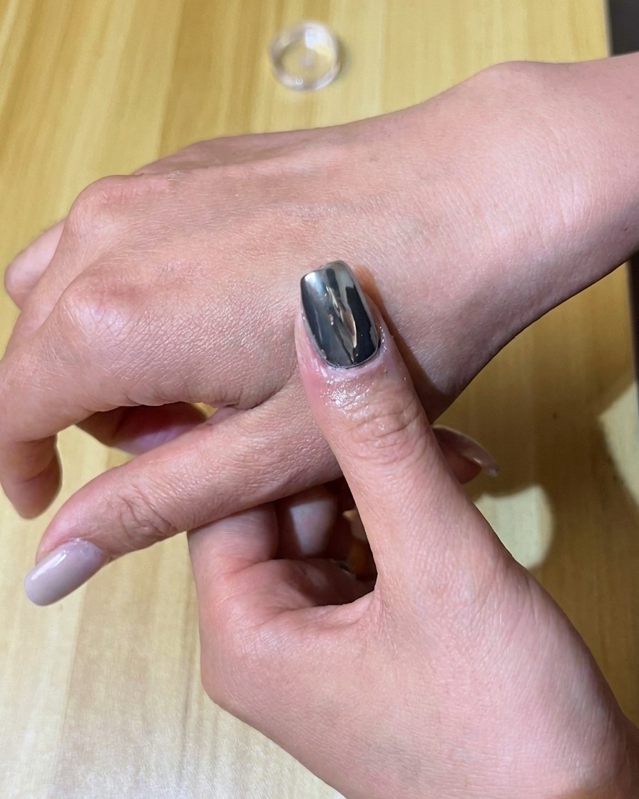 A sponge applicator rubbing silver chrome pigment onto a black gel-painted nail.