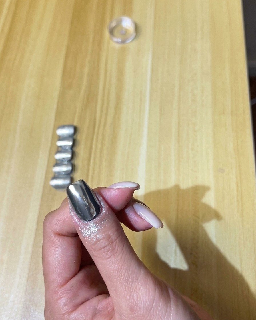 A fluffy makeup brush gently brushing off extra silver chrome powder from the nail.