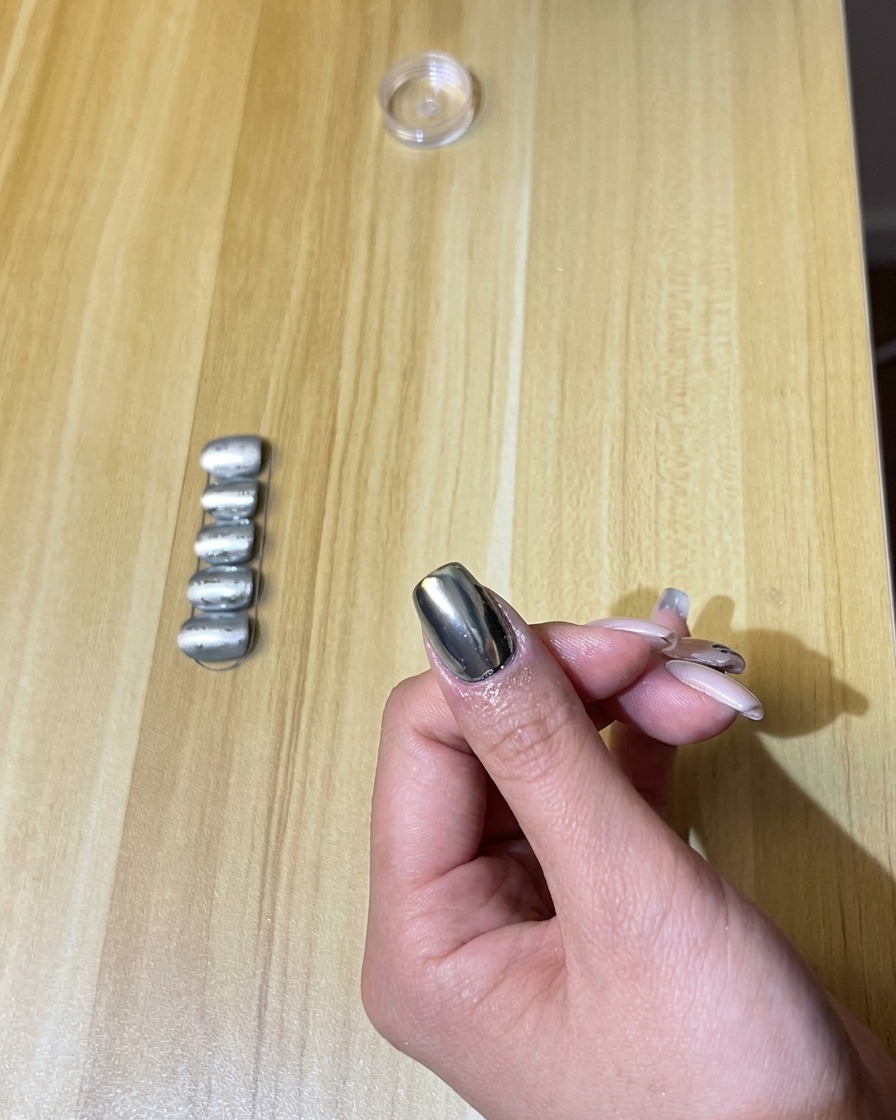 A hand with chrome-finished nails inside a UV/LED nail lamp, with the light turned on.