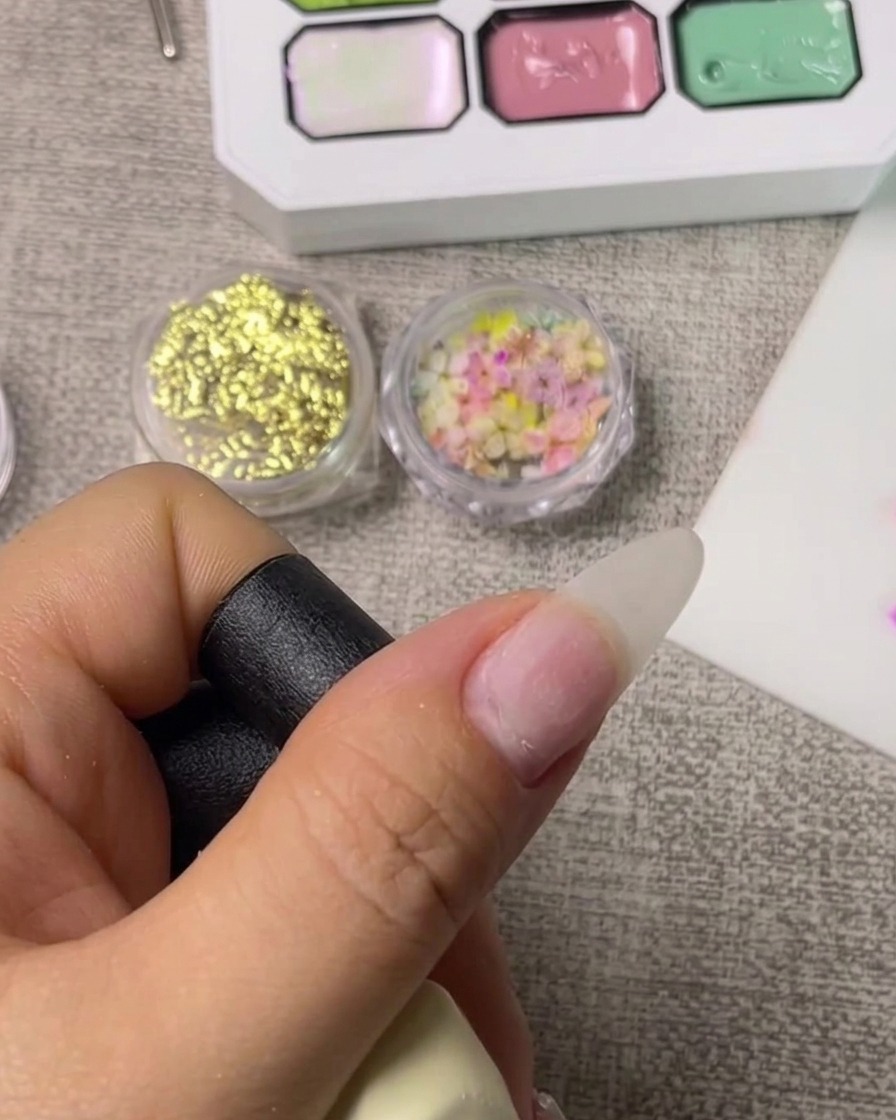 A close-up view of a brush applying a clear base coat to a clean natural fingernail.