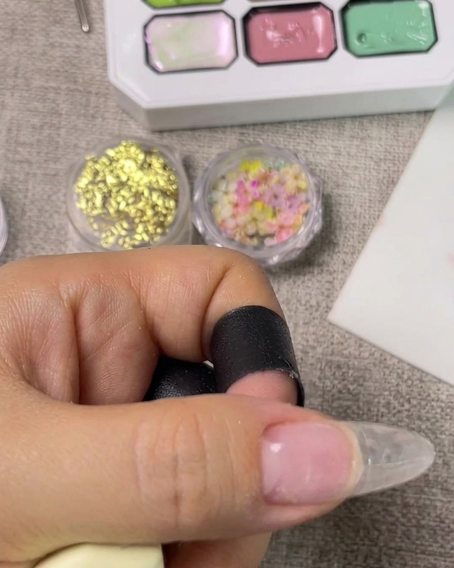 A hand placed inside a UV nail lamp with the light activated, curing the base coat.