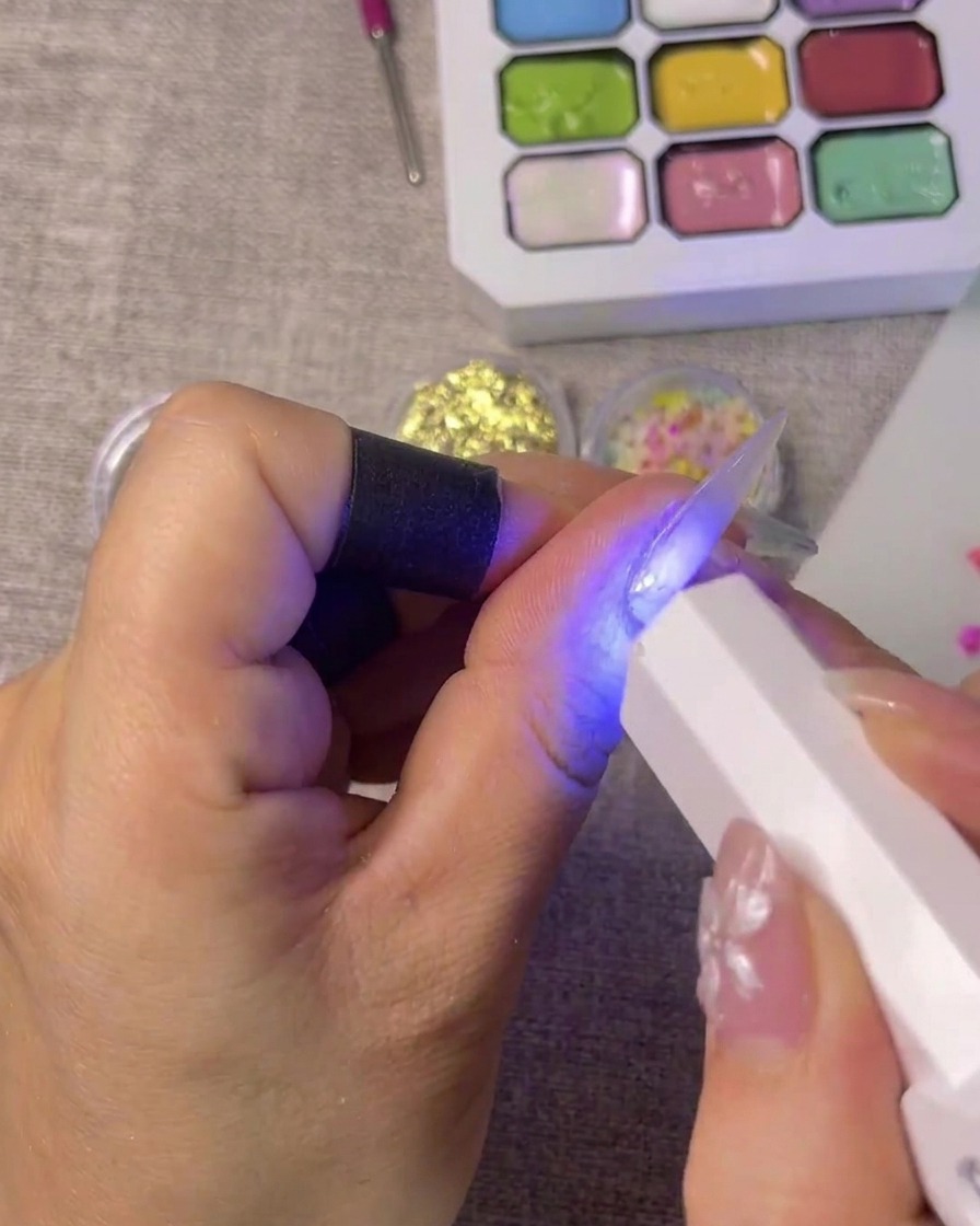 A French tip sticker being precisely positioned on the tip of a fingernail.