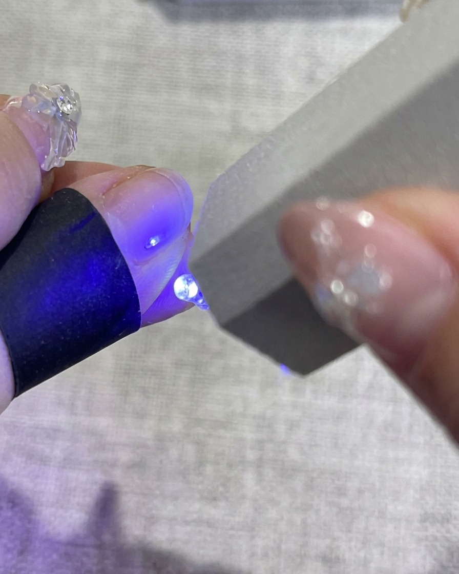 A hand with decorated floral nails placed inside a UV nail lamp, with the blue light emitting from the machine to cure the polish.