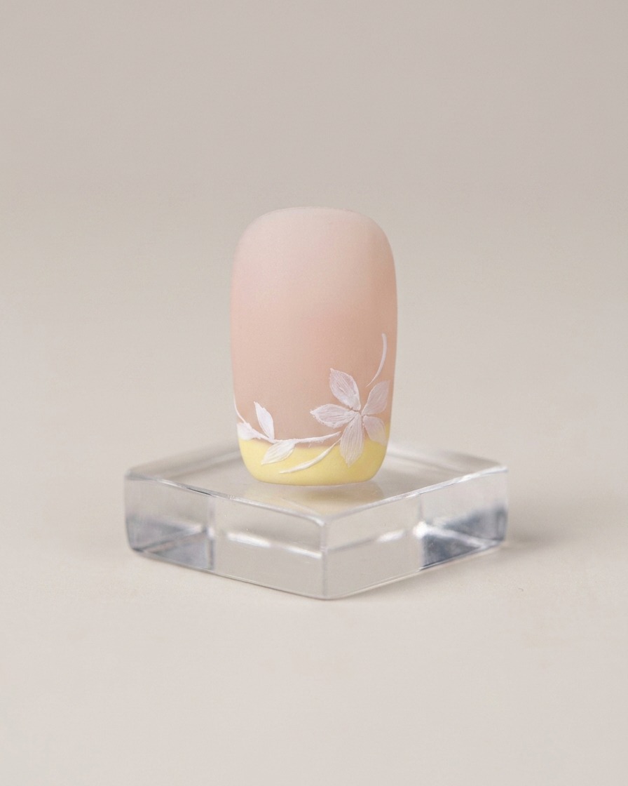 A brush applying a smooth layer of light nude gel base coat to a natural nail plate.