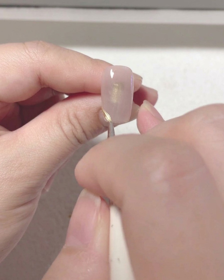 A thin nail art brush drawing a neat red French tip line on the edge of a nail.