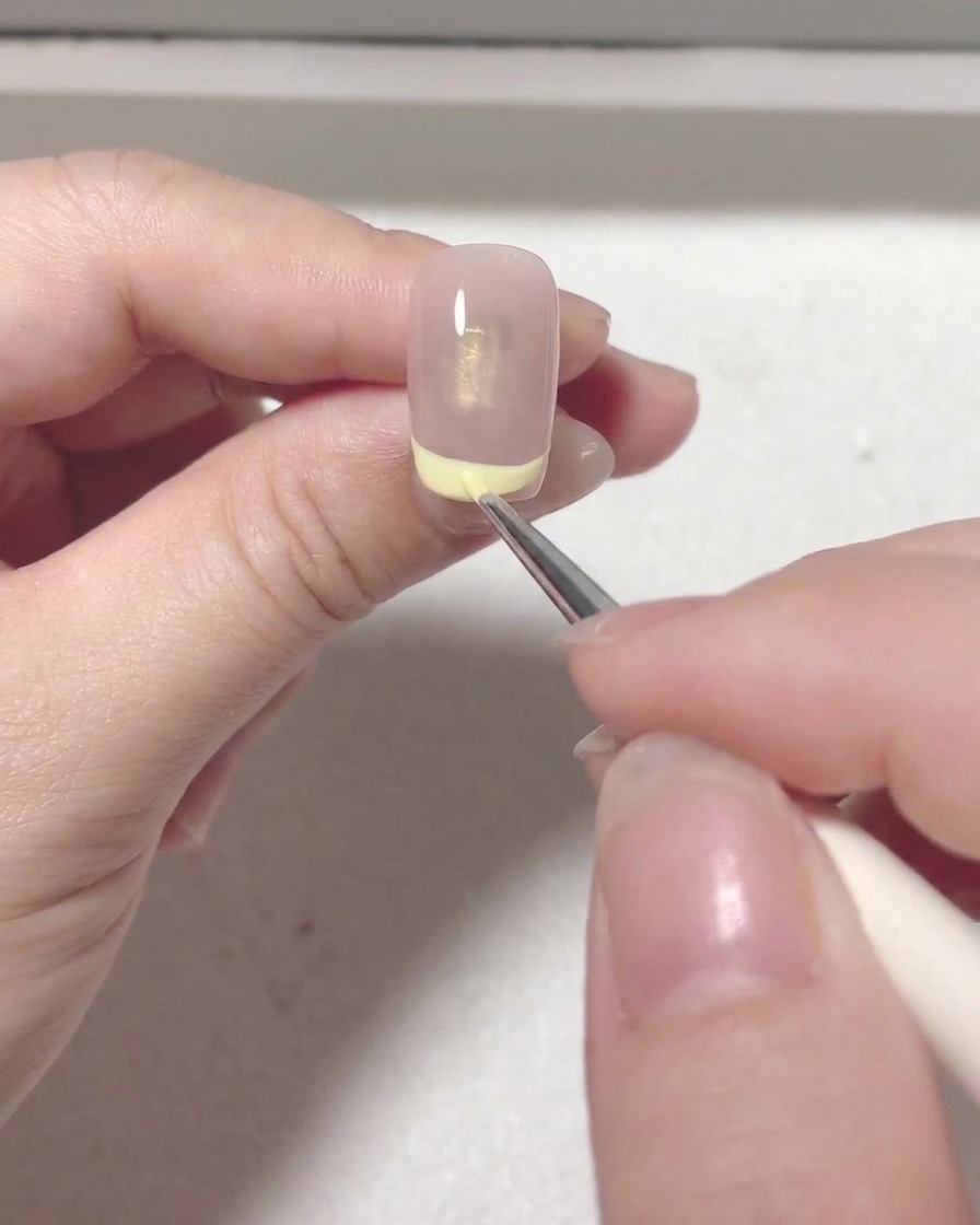 A detail brush filling in the red color within the French tip line on a nail.