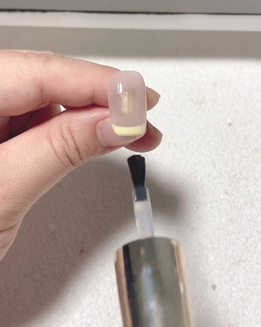 A brush applying a clear matte top coat over the fully painted red French tip nail.