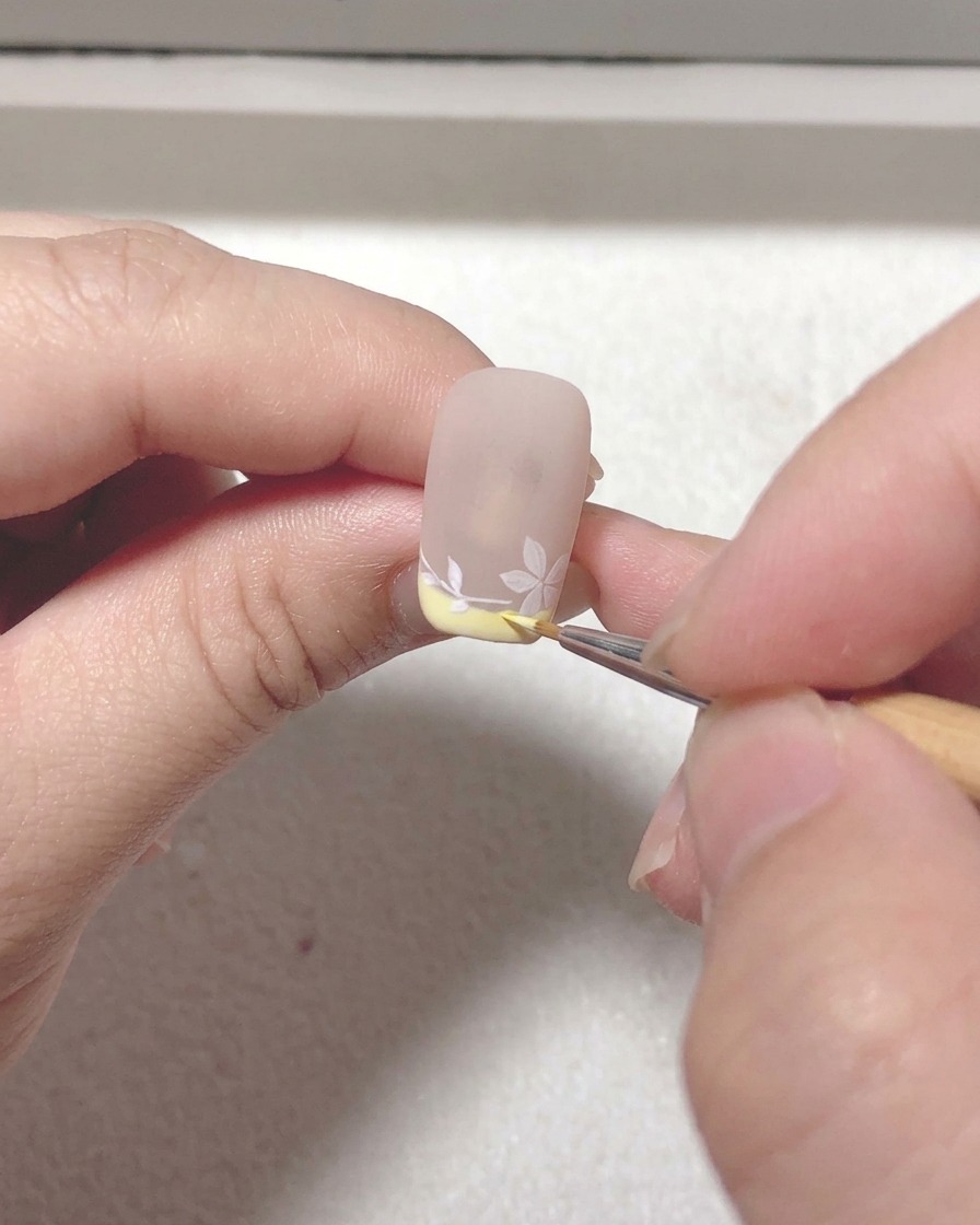 A close-up of a liner brush adding final touches and refining lines on the sakura nail art design.