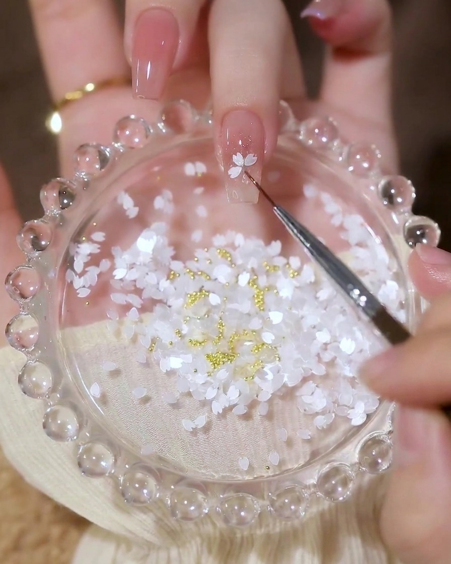 A close-up of a detailing brush placing white petal-shaped sequins onto a nail in a flower pattern.