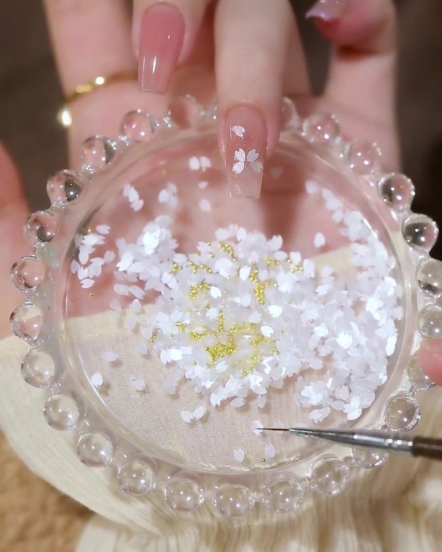 A nail with a completed flower design made of petal sequins, with a small gold center bead.