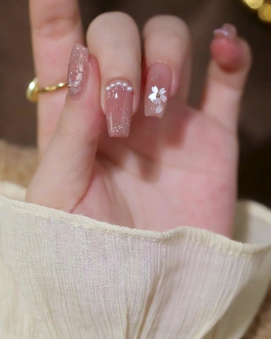 Small, white half-pearls being placed in a row along the cuticle line of a fingernail.