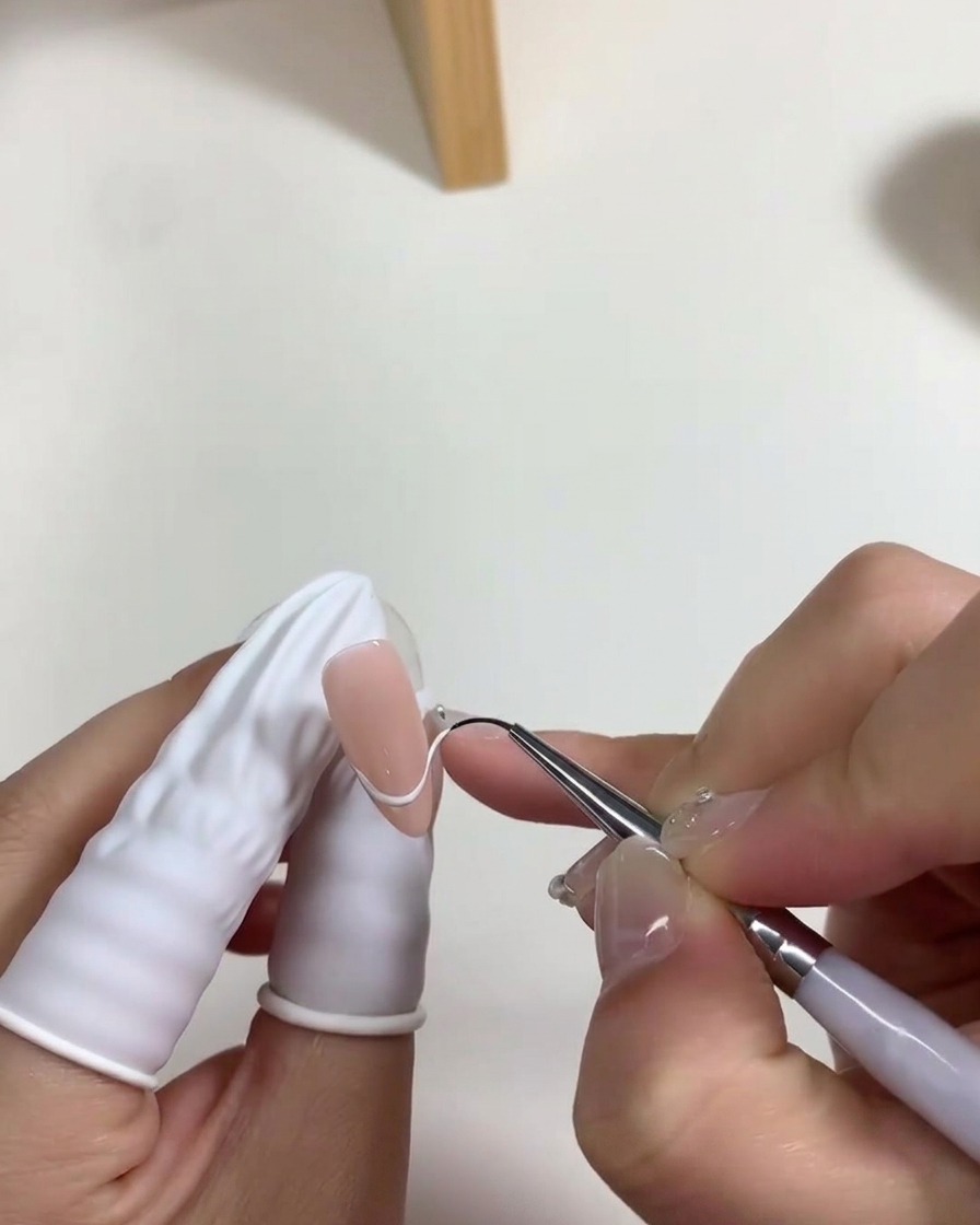 A nail brush applying a thin layer of milky white gel polish to the nail bed.