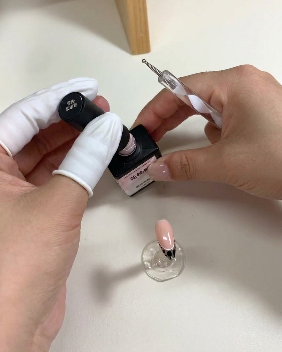 A dotting tool placing five pink gel dots on a nail surface to create a flower shape.